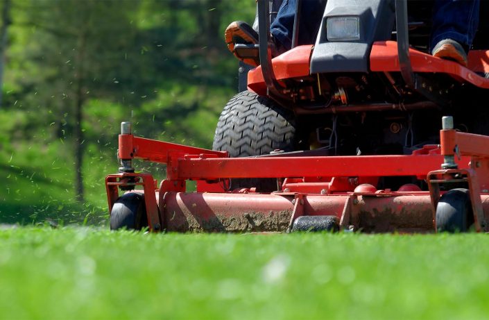 A person on a red lawn mower in the grass.