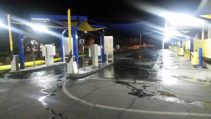 A gas station with lights on and a car parked in the background.