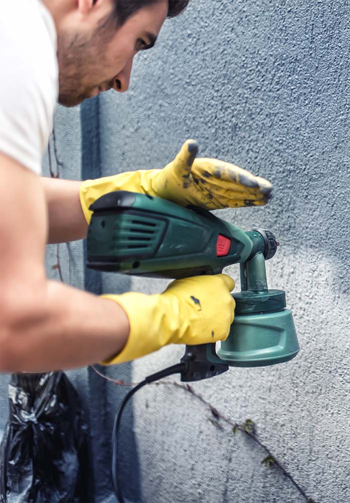 A person in yellow gloves holding a paint gun.